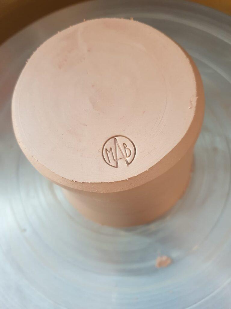 Vue de dessus d'une pièce en terre cuite avec un logo gravé dans la matière. Technique Céramique .